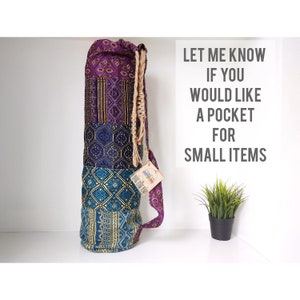 May include: A colourful yoga mat bag with a drawstring closure and a long strap. The bag is made of patchwork fabric with different patterns in shades of purple, blue, and gold. The text "Let me know if you would like a pocket for small items" is written in white on a white background.