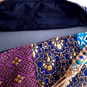 May include: A colorful yoga mat bag with a zippered pocket and a tassel with beads. The bag is made of a patchwork of fabrics with floral and geometric patterns in shades of purple, blue, gold, and turquoise.