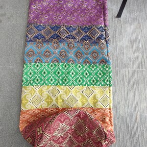 May include: A colorful yoga mat bag with a drawstring closure. The bag is made of a patterned fabric with stripes of purple, blue, green, yellow, orange, and red.