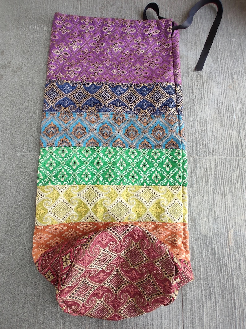 May include: A colorful yoga mat bag with a drawstring closure. The bag is made of a patterned fabric with stripes of purple, blue, green, yellow, orange, and red.