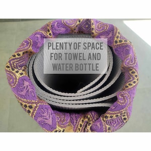 Może przedstawiać: Zwinięta mata do jogi z pokryciem z tkaniny w kolorze fioletowym i złotym. Na pokryciu nadrukowany jest tekst "PLENTY OF SPACE FOR TOWEL AND WATER BOTTLE".