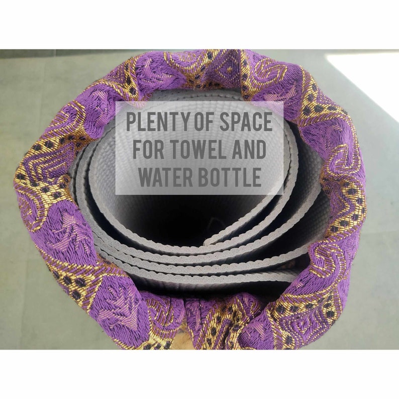 Może przedstawiać: Zwinięta mata do jogi z pokryciem z tkaniny w kolorze fioletowym i złotym. Na pokryciu nadrukowany jest tekst "PLENTY OF SPACE FOR TOWEL AND WATER BOTTLE".