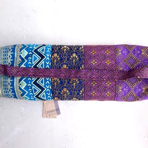 May include: A purple, blue, and gold yoga mat bag with a patchwork design. The bag has a strap and the text "COSMOCITY" is printed on a tag attached to the bag.