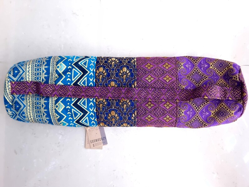 May include: A purple, blue, and gold yoga mat bag with a patchwork design. The bag has a strap and the text "COSMOCITY" is printed on a tag attached to the bag.