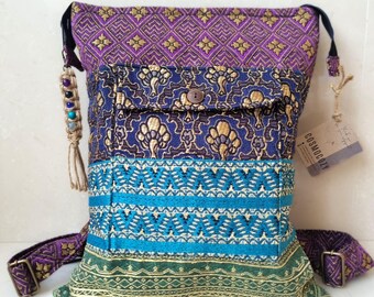 May include: A multi-colored patchwork crossbody bag with a purple, blue, green, and gold pattern. The bag has a flap with a button closure and a small pocket on the front. The bag has a long adjustable strap and a small tassel on the side. The bag has a tag that says "COSMOGROOVY".