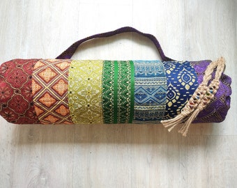 May include: A colorful yoga mat bag with a rainbow design. The bag features a variety of patterns and colors, including red, orange, yellow, green, blue, and purple. It has a woven handle and a decorative tassel.