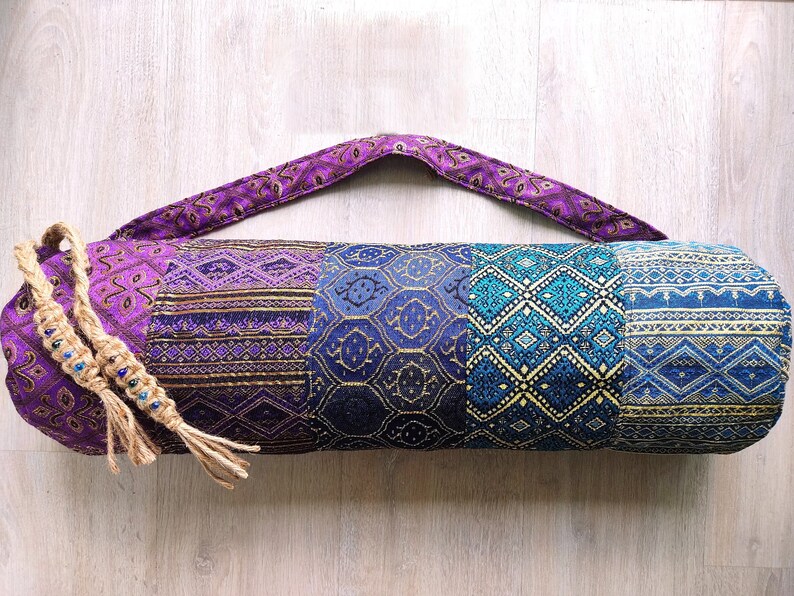 May include: A purple and blue yoga mat bag with a patterned design. The bag has a long strap and a drawstring closure.