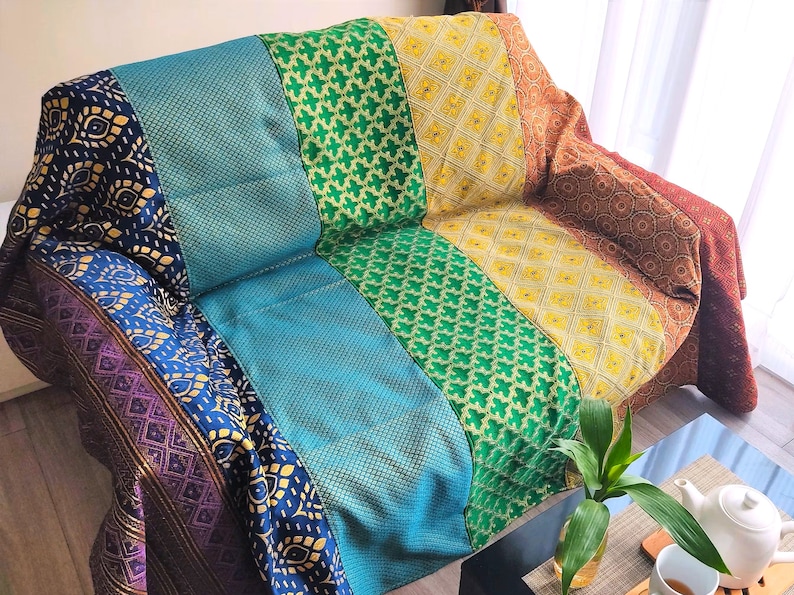 May include: A colorful couch throw with a patchwork design featuring shades of purple, blue, green, yellow, and brown. The throw is made of a soft, textured fabric and has a geometric pattern.
