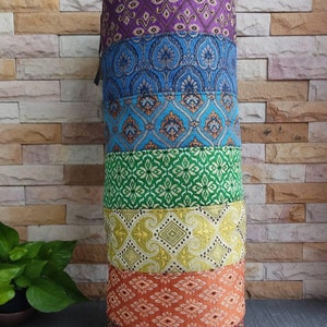 May include: A cylindrical meditation cushion with a colorful patchwork design. The cushion is made of fabric with different patterns in shades of purple, blue, green, yellow, orange, and red.