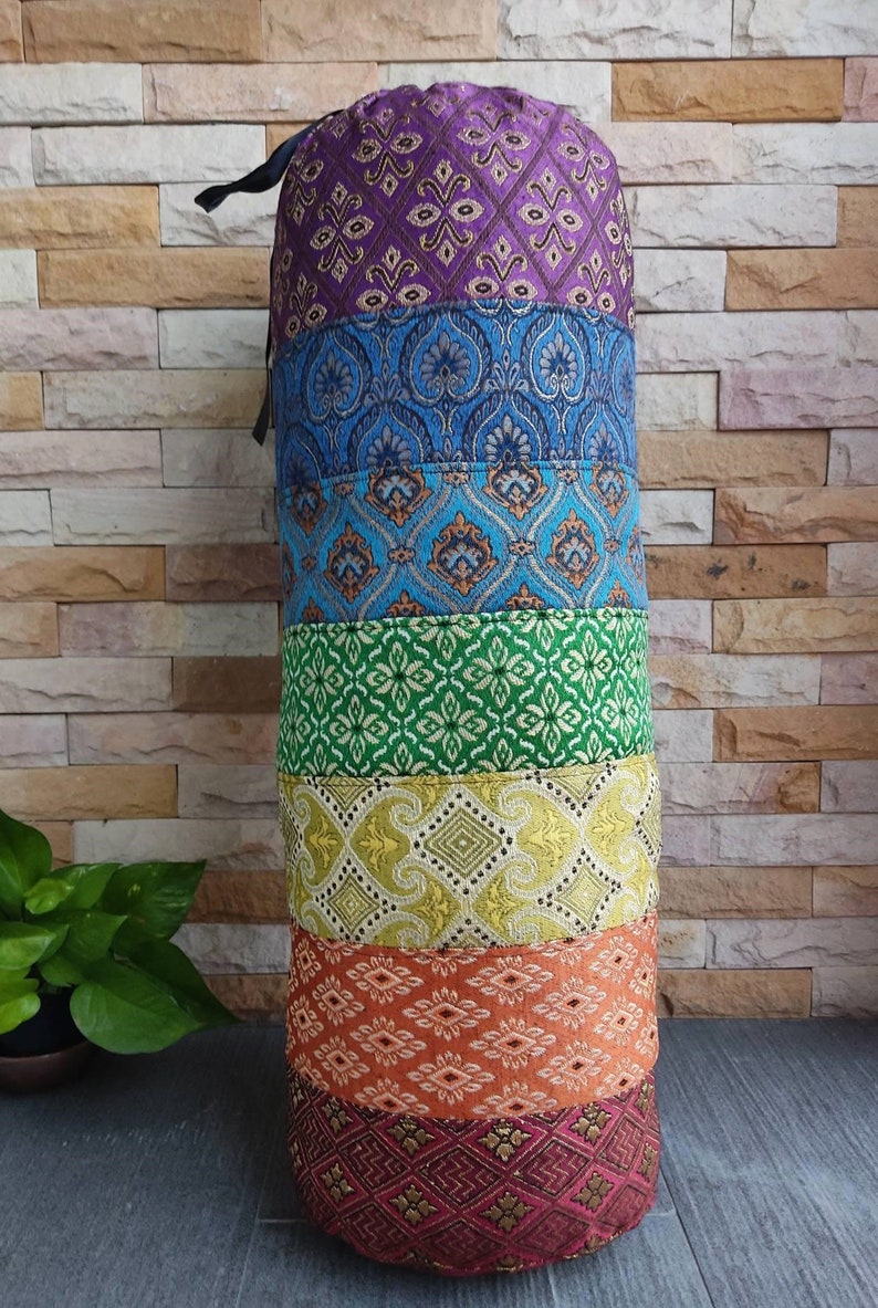 May include: A cylindrical meditation cushion with a colorful patchwork design. The cushion is made of fabric with different patterns in shades of purple, blue, green, yellow, orange, and red.