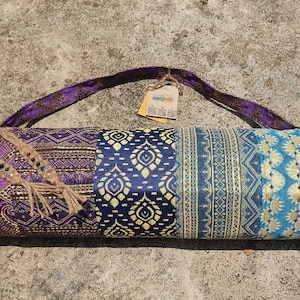 May include: A purple, blue, and teal yoga mat bag with a gold and blue patterned design. The bag has a purple strap and a brown tassel.