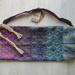 May include: Purple, blue and gold yoga mat bag with a woven strap and tassels. The bag has a geometric pattern.