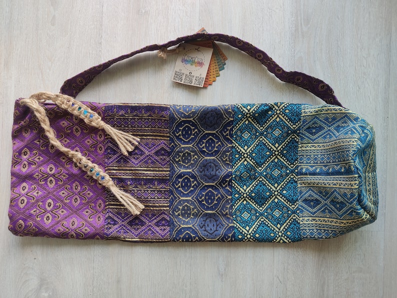 May include: Purple, blue and gold yoga mat bag with a woven strap and tassels. The bag has a geometric pattern.