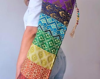 May include: A colorful yoga mat bag with a rainbow design. The bag is made of patterned fabric in shades of red, orange, yellow, green, blue, and purple. It has a beaded tassel and is carried over the shoulder.