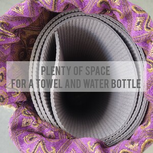 May include: A rolled-up grey yoga mat with a purple and gold patterned fabric cover. The text "PLENTY OF SPACE FOR A TOWEL AND WATER BOTTLE" is visible on the image.