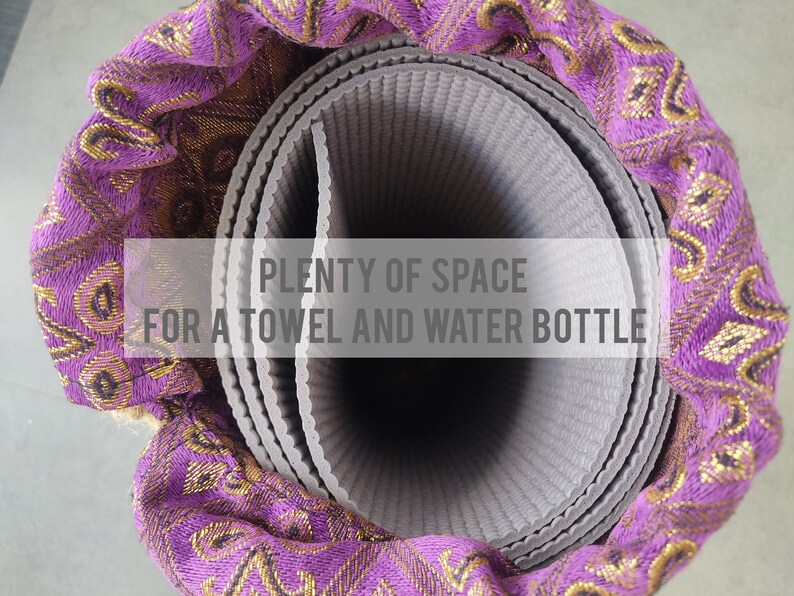 May include: A rolled-up grey yoga mat with a purple and gold patterned fabric cover. The text "PLENTY OF SPACE FOR A TOWEL AND WATER BOTTLE" is visible on the image.