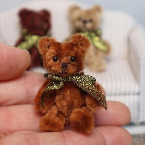 Może przedstawiać: Mały brązowy miś pluszowy z zielono-złotą kokardką. Miś siedzi w dłoni osoby.