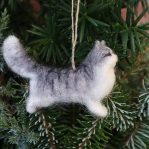 Może przedstawiać: Szary i biały filcowy ornament w kształcie kota wiszący na zielonej choince.