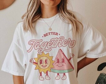 May include: White oversized t-shirt with a graphic of a smiling sun and watermelon holding hands. The text "Better Together" is printed above the graphic.