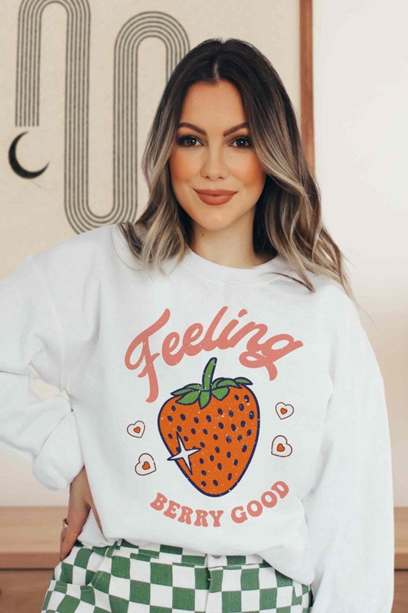 May include: White sweatshirt with a pink graphic of a strawberry and the text "Feeling Berry Good".