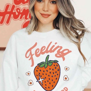 May include: White sweatshirt with a red strawberry graphic and the text "Feeling Berry Good".