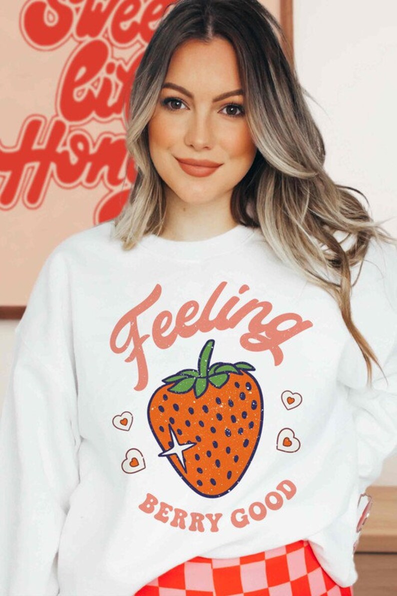 May include: White sweatshirt with a red strawberry graphic and the text "Feeling Berry Good".