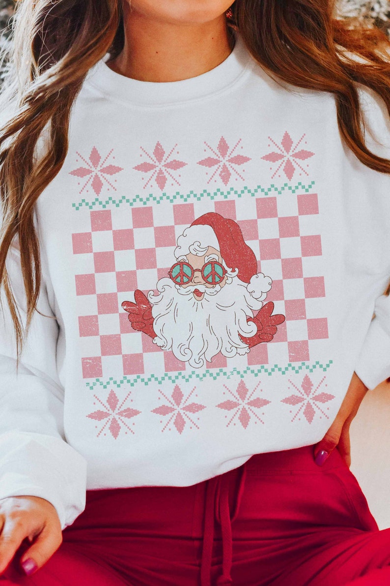 K&ouml;nnte beinhalten: Wei&szlig;er Weihnachtspullover mit einem rosa-gr&uuml;nen Karomuster, Schneeflocken und einem Retro-Weihnachtsmann mit Peace-Zeichen-Sonnenbrille.