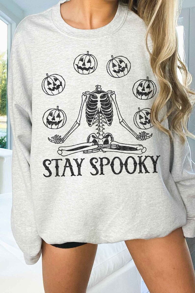 May include: A gray sweatshirt with a skeleton meditating and holding pumpkins. The text "STAY SPOOKY" is printed below the skeleton.