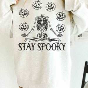 May include: A gray sweatshirt with a skeleton meditating with pumpkins around it. The text "STAY SPOOKY" is printed below the skeleton.