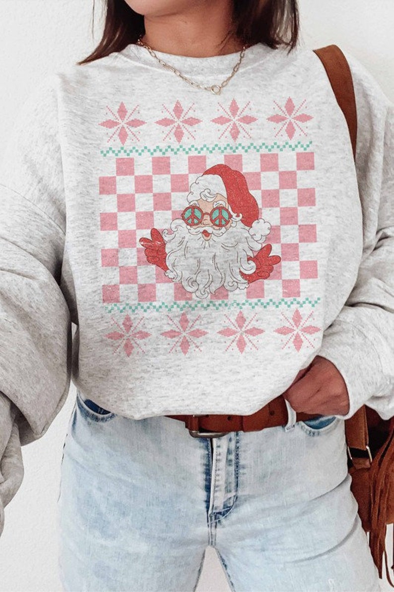 K&ouml;nnte beinhalten: Ein grauer Pullover mit einem rosa und gr&uuml;nen Karomuster und einem Cartoon-Weihnachtsmann, der eine Peace-Sign-Sonnenbrille tr&auml;gt. Der Weihnachtsmann tr&auml;gt einen roten Hut und einen wei&szlig;en Bart.