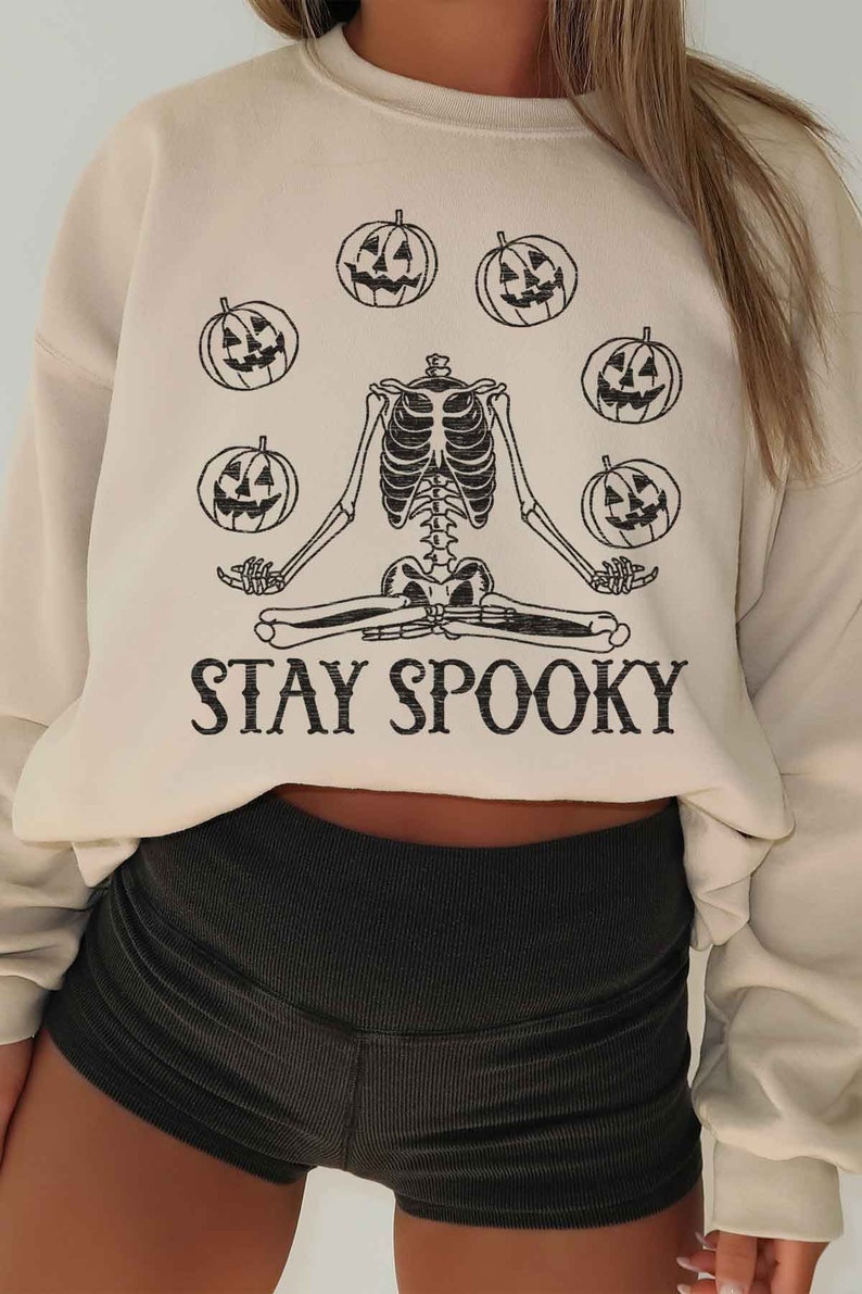 May include: A beige sweatshirt with a skeleton meditating with pumpkins around it. The text "STAY SPOOKY" is printed below the skeleton.