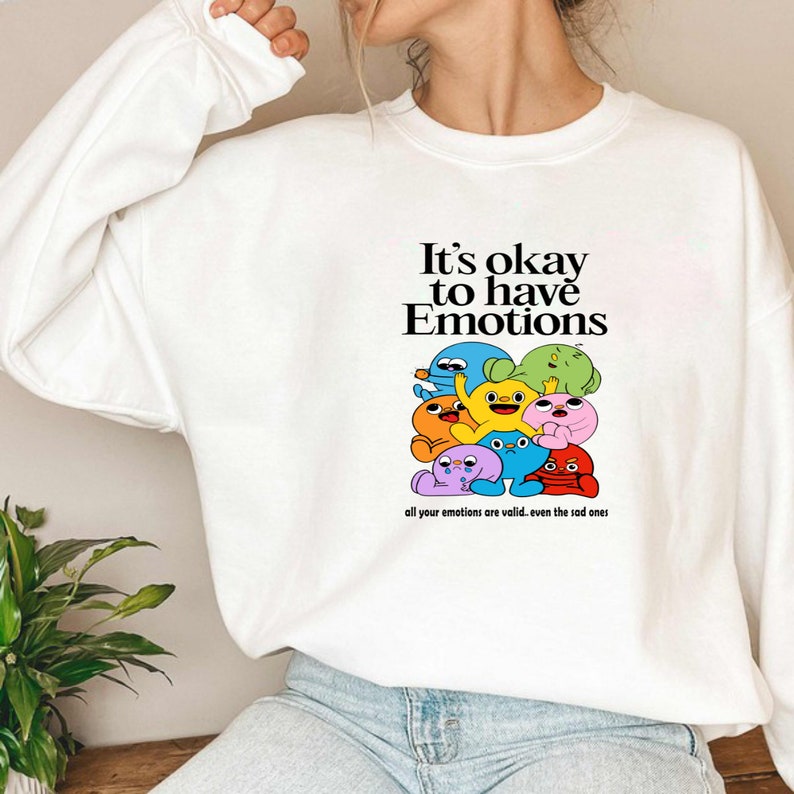 Peut inclure: Sweat-shirt blanc avec un motif de personnages de dessins anim&eacute;s color&eacute;s et le texte "It's okay to have Emotions. All your emotions are valid. Even the sad ones."