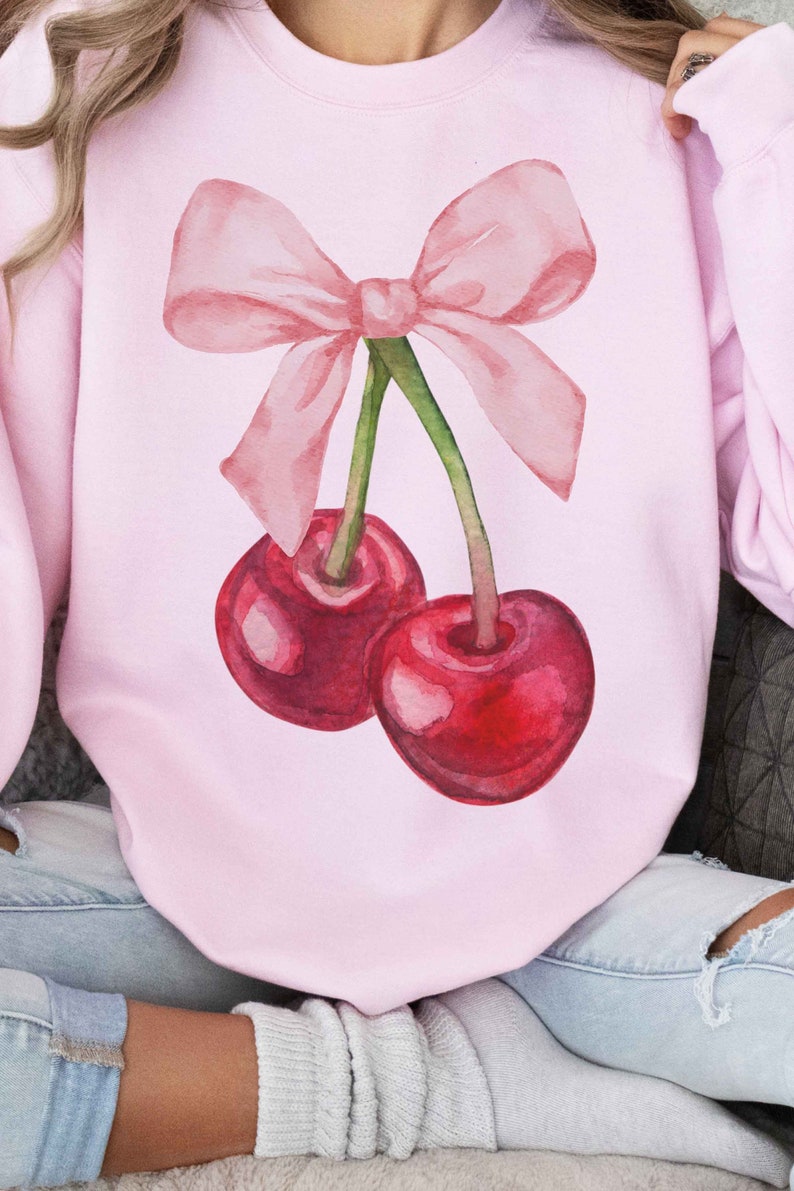 May include: A pink sweatshirt with a watercolor illustration of two cherries with a pink bow on top.