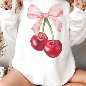 May include: White sweatshirt with a pink bow and two red cherries printed on the front.