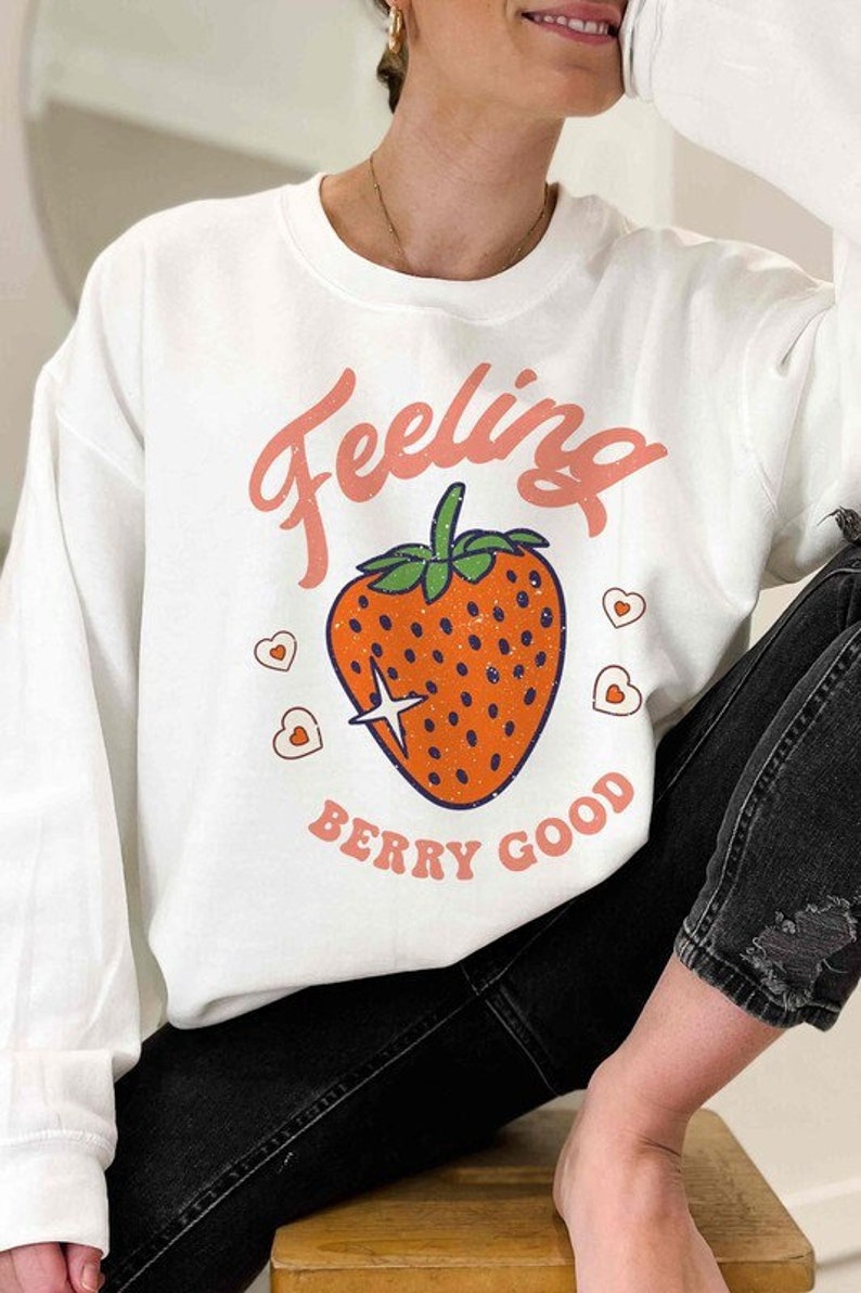 May include: White sweatshirt with a pink graphic of a strawberry and the text "Feeling Berry Good".