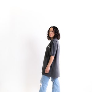 May include: A person wearing a dark gray oversized t-shirt with a white graphic print and light blue jeans with distressed details. They are wearing beige platform shoes.