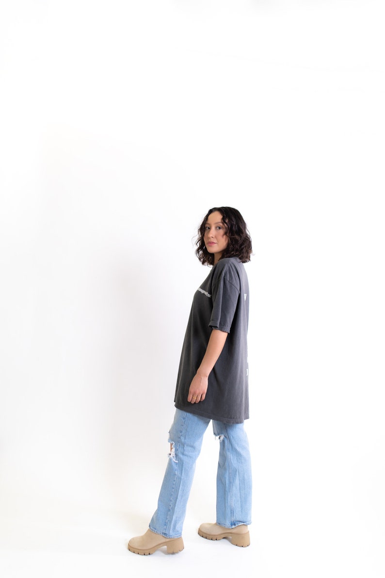 May include: A person wearing a dark gray oversized t-shirt with a white graphic print and light blue jeans with distressed details. They are wearing beige platform shoes.