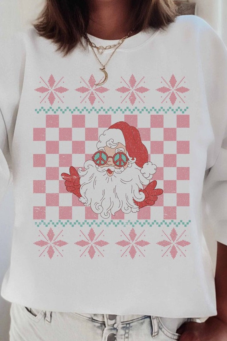 K&ouml;nnte beinhalten: Wei&szlig;er Weihnachtspullover mit einem rosa-gr&uuml;nen Karomuster und einem Cartoon-Weihnachtsmann mit Peace-Zeichen-Sonnenbrille. Der Pullover hat ein festliches Schneeflockenmuster.