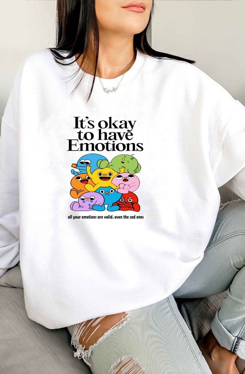Peut inclure: Sweat-shirt blanc avec un motif de personnages de dessins anim&eacute;s color&eacute;s et le texte "It's okay to have Emotions. All your emotions are valid... even the sad ones."
