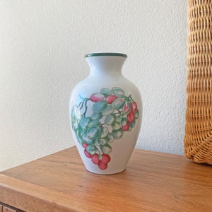 Peut inclure: Vase en céramique blanche avec un bord vert et un motif peint de raisins verts et de baies roses.