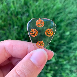May include: A clear, heart-shaped guitar pick with three orange glitter pumpkin faces.