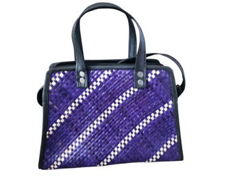 May include: A woven handbag with a purple and white diagonal pattern. The bag has black leather handles and trim, with silver-colored rivets. It includes a shoulder strap and a zipper closure.