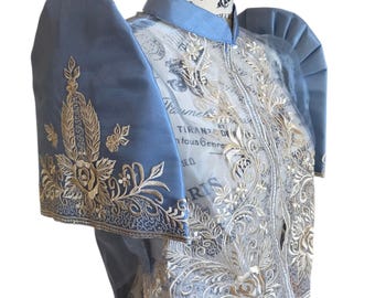 May include: A light blue top with intricate gold embroidery and sheer overlay. The sleeves are puffed and adorned with floral patterns. The top has a high collar and a delicate, ornate design, showcasing a blend of textures and colors.