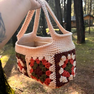 May include: A crocheted tote bag with a brown, green, and orange granny square pattern. The bag has two handles and is made with a beige yarn.