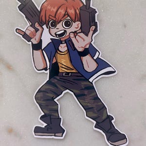 Könnte beinhalten: Ein Aufkleber mit einer Zeichentrickfigur mit orangefarbenem Haar, die zwei schwarze Spielzeugpistolen hält. Die Figur trägt eine blaue Jacke, ein gelbes Hemd, eine Camouflage-Hose und schwarze Stiefel. Die Figur macht eine Rock'n'Roll-Handgeste.