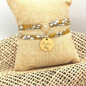 Joli bracelet en tissu, orné d'un cœur doré, prêt à être personnalisé selon vos souhaits. Il peut être porté ajusté grâce à des nœuds coulissants.