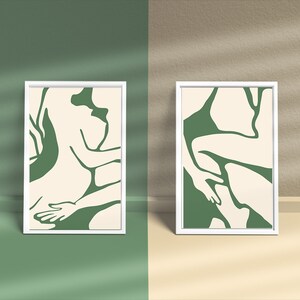 Op de afbeelding: Twee ingelijste prints met abstracte lijntekeningen van figuren in groen en cr&egrave;me kleuren. De prints zijn in witte lijsten en hangen aan een muur.