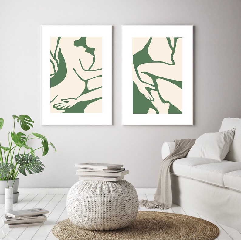 Op de afbeelding: Twee abstracte kunstprints met een groene achtergrond en witte contouren van figuren. De prints zijn wit ingelijst en hangen aan een witte muur.
