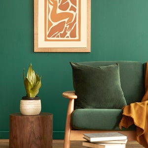 May include: A green velvet sofa with a brown throw blanket and a wooden side table with a potted plant. A framed print with an abstract design hangs on the wall behind the sofa.