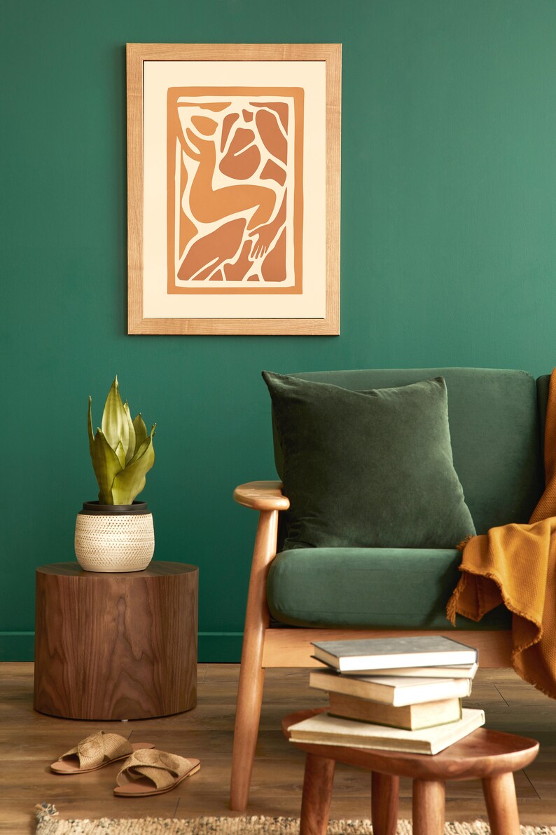 May include: A green velvet sofa with a brown throw blanket and a wooden side table with a potted plant. A framed print with an abstract design hangs on the wall behind the sofa.